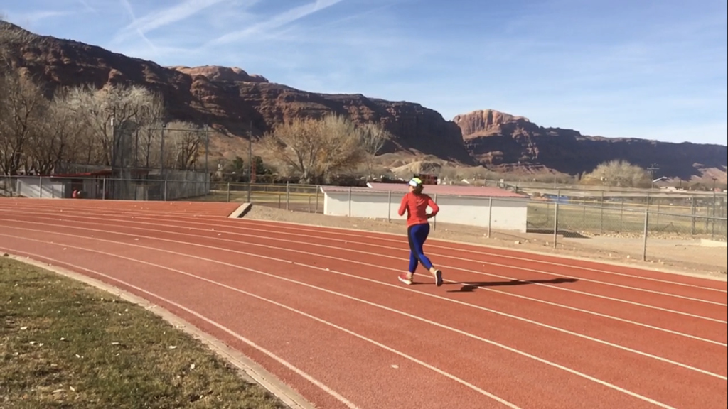 Lucy runs around the track on the last lap of the Winter Sun 10k with the Moab rim in the background
